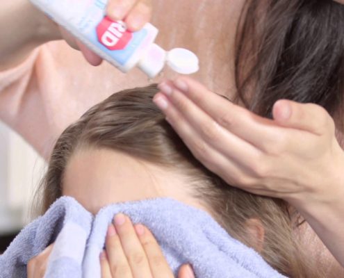 LCA Technician putting ointment into a young girls hair who has been infested with lice as she covers her eyes with a towel